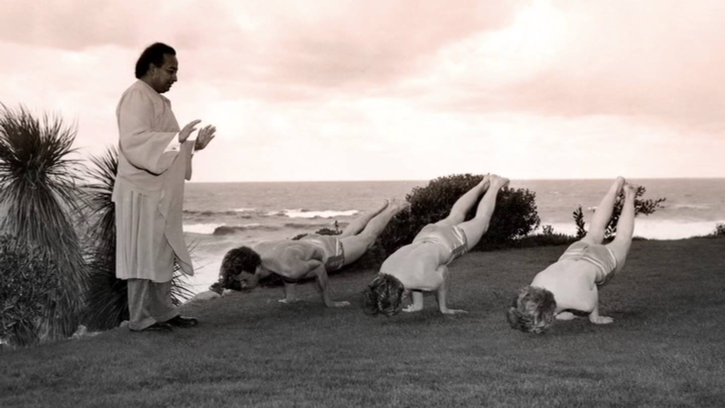 foto in bianco e nero , yogananda guarda 2 studenti che fanno un esercizio sulle braccia, una flessione con le gambe alzate dietro.