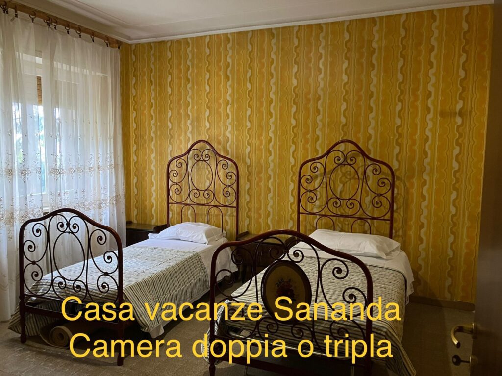 foto, camera da letto doppia , i letti in ferro  battuto,  la carta da parati di colore giallo con striature arancio e marrone  chiaro.  